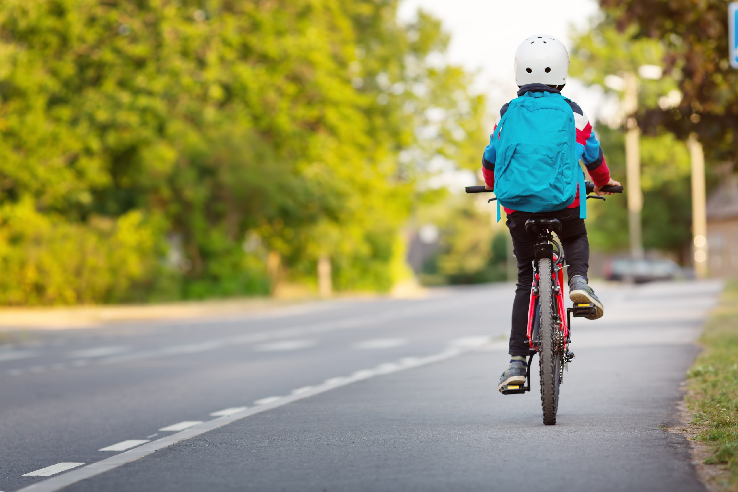 Child with rucksack riding on bikes in the park near school. Pupil with backpack outdoors