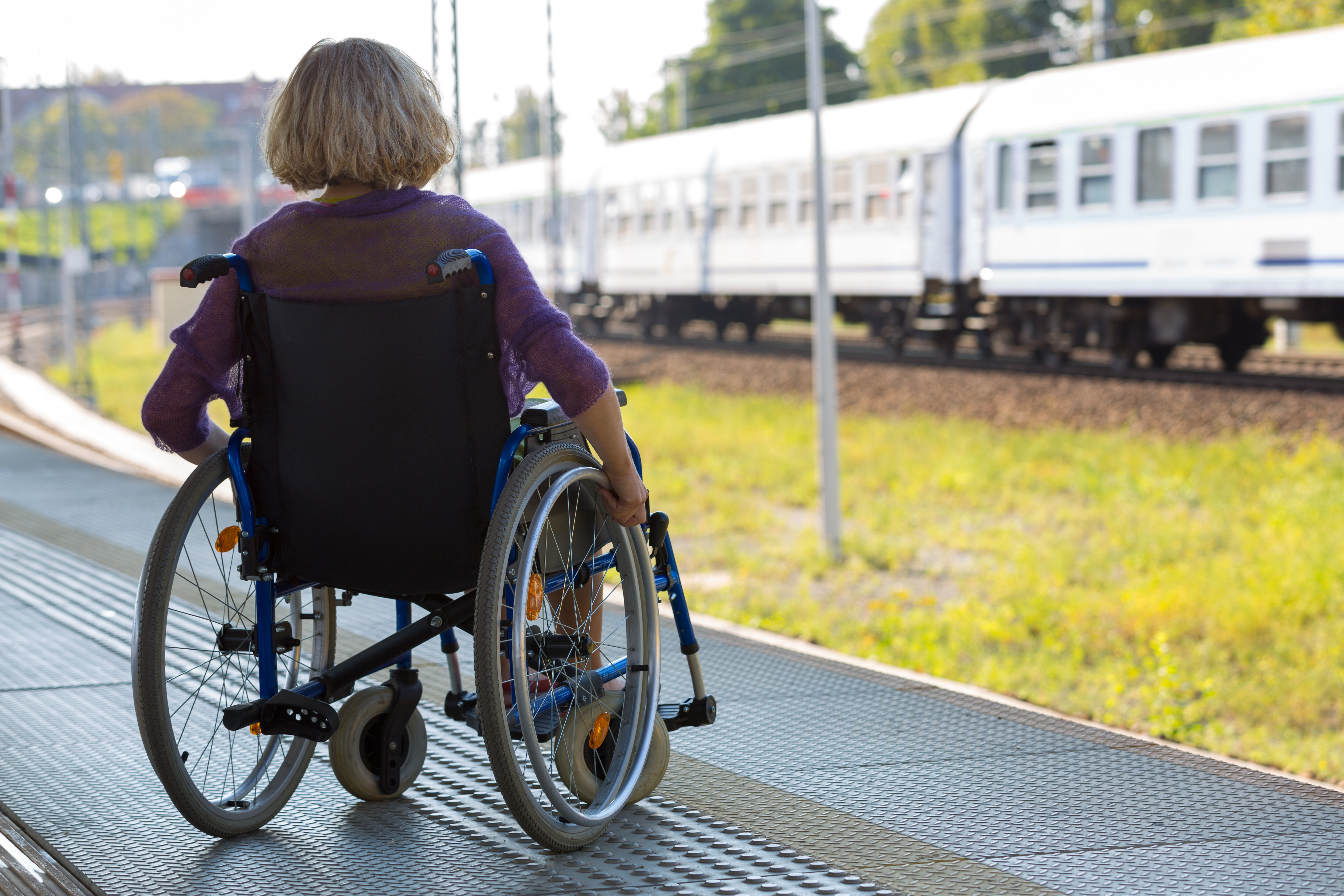 lonely woman sitting on wheelchair on a train platform watching the train passing by, back view